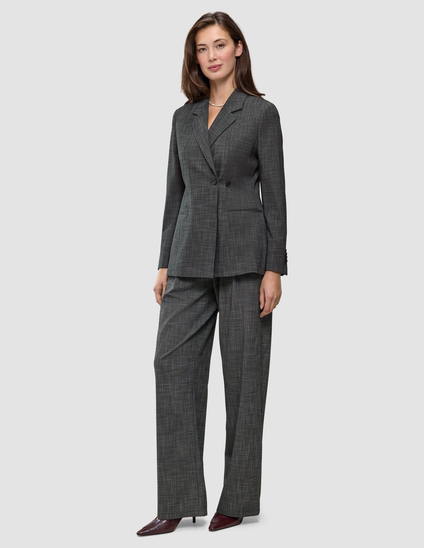 En kvinne har på seg en Women Nara Blazer Fitted Black Check i mørkegrå rutemønster, sammen med matchende bukser med vid benåpning og 360°-stretch.